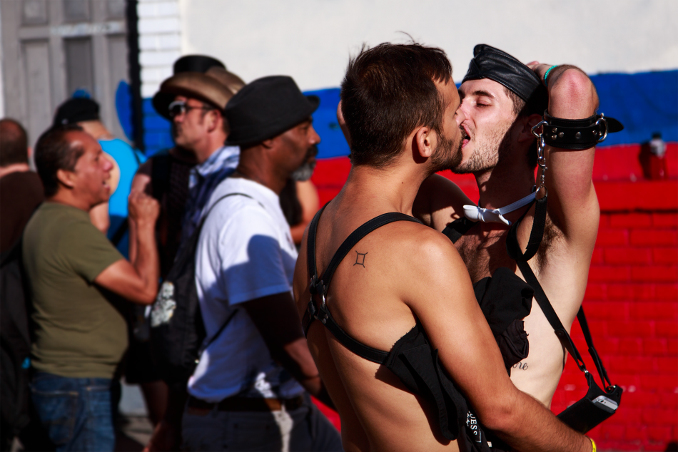 Photo of 2 folks making out at Up Your Alley with folks walking in background.